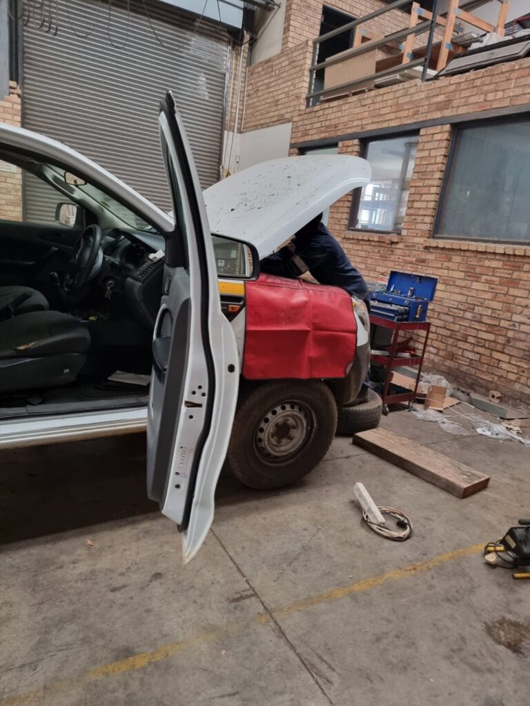 Mechanical work on a white bakkie with its bonnet open at a business premises